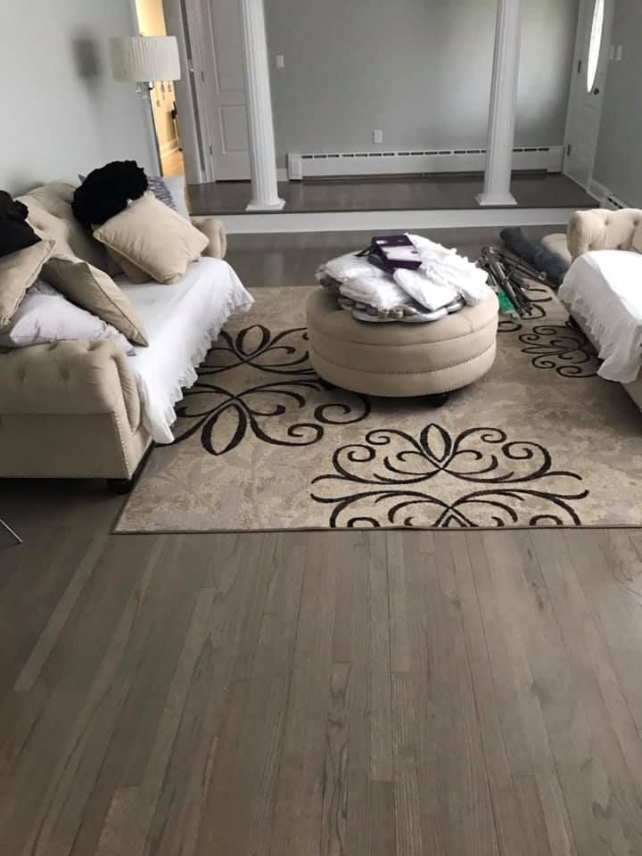 Beige living room with light wood floor, patterned rug, tufted sofas, and round ottoman.