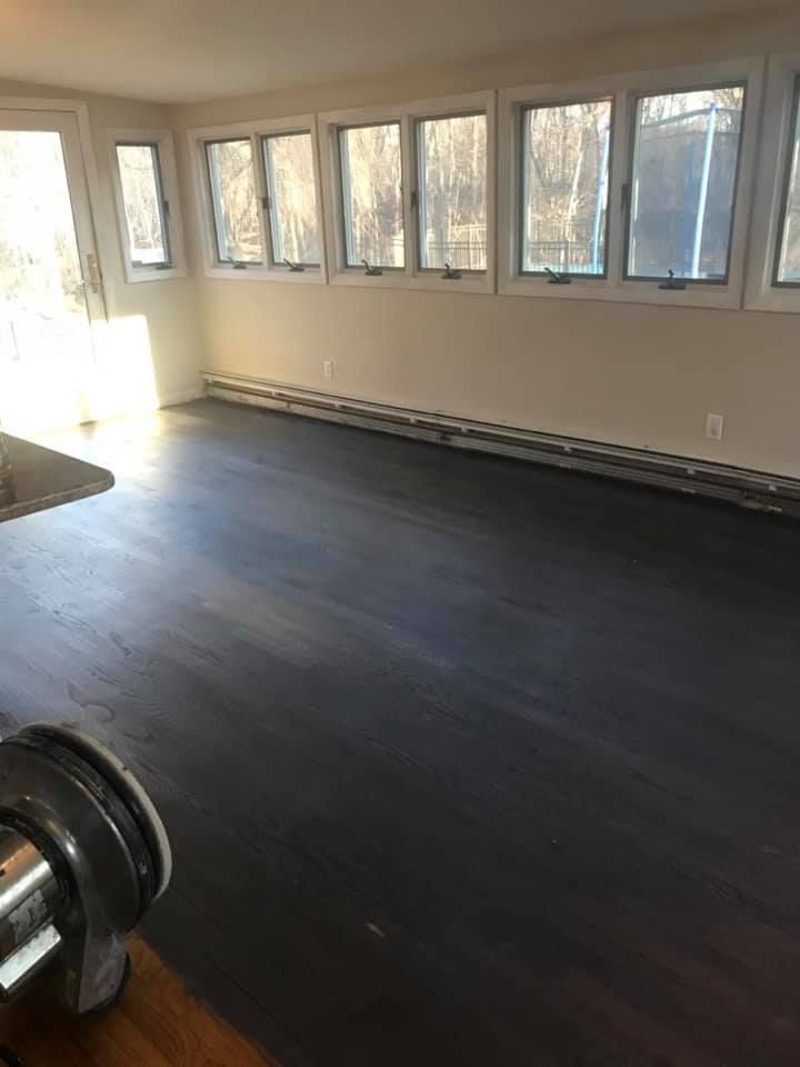 A room with dark stained wooden floors, many windows, and white walls.