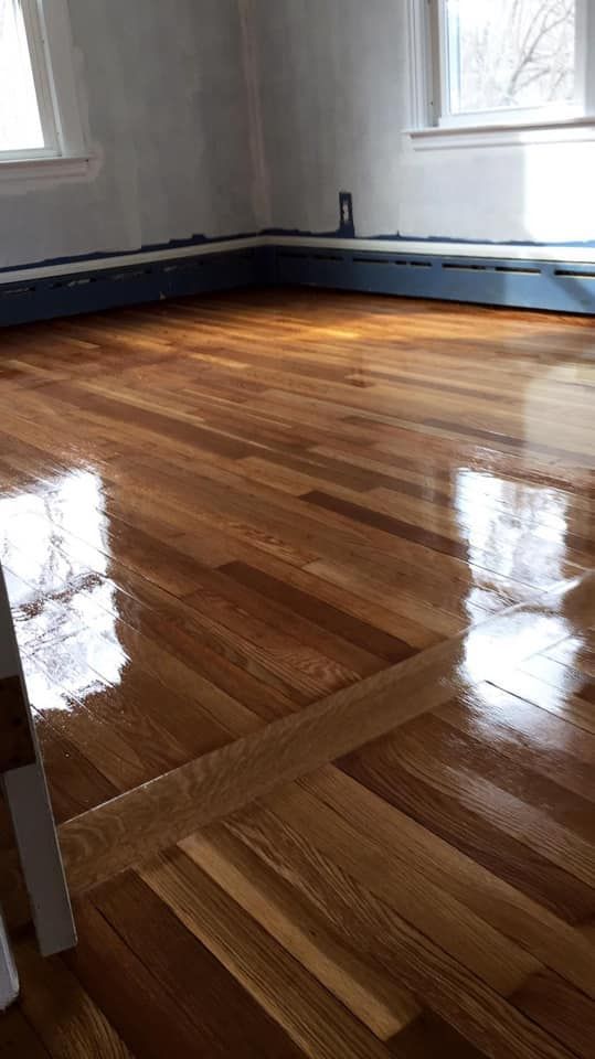 Refinished hardwood floor reflecting light; room with blue baseboard and windows.