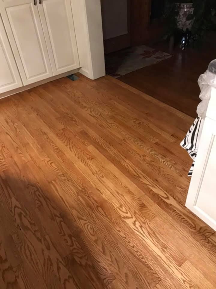 Hardwood floor in a kitchen, leading towards a doorway, near white cabinets.