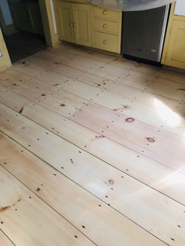 Newly refinished light wood floor in a kitchen with yellow cabinets and a dishwasher.