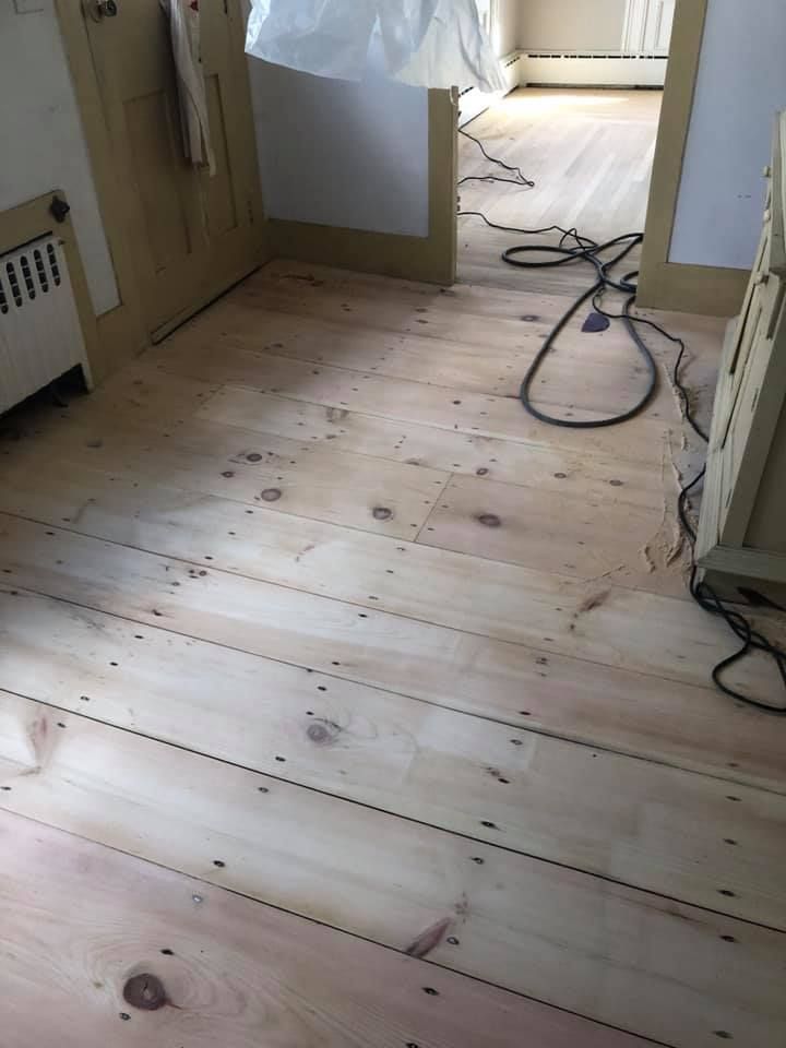 Light wooden floorboards in a doorway; electrical cords strewn; sunlight streams in from another room.