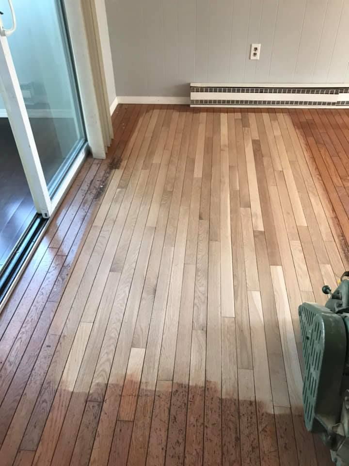 Hardwood floor being sanded; half light wood, half dark stained, machine on the right.