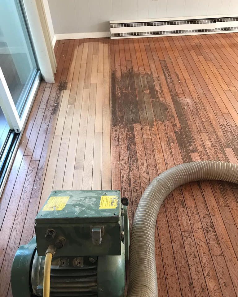 Floor sanding machine working on a wooden floor; one section is sanded, and another is not.