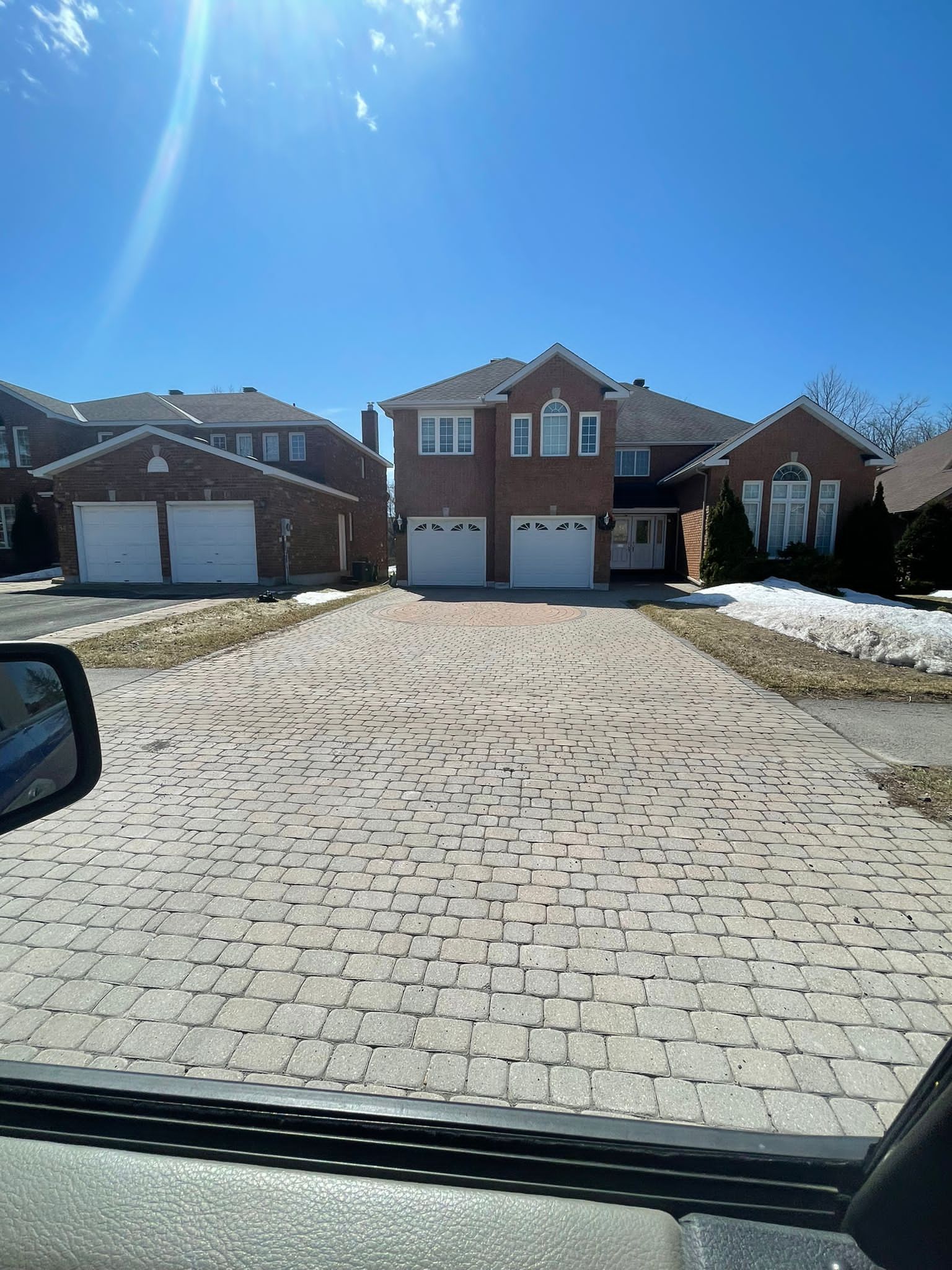 Two-story brick house with two-car garage, brick driveway, and blue sky.