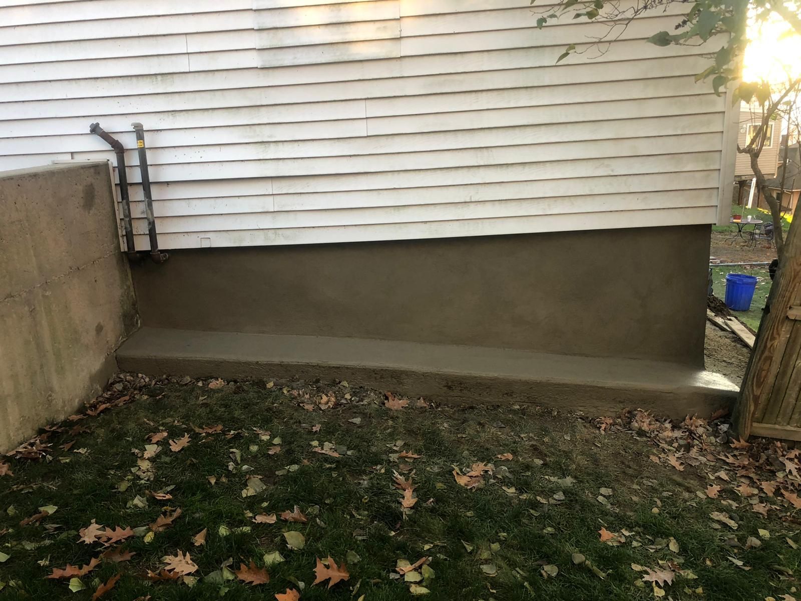 Concrete foundation of a building, with freshly applied cement on a lower portion; exterior shot.