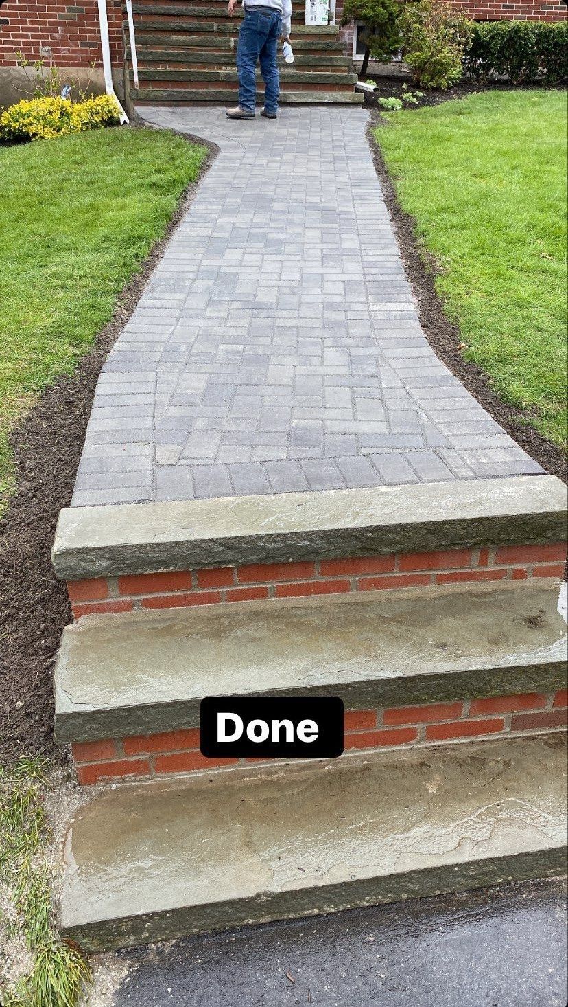 Brick pathway leads to the front door, past the steps. A person stands by the entrance.