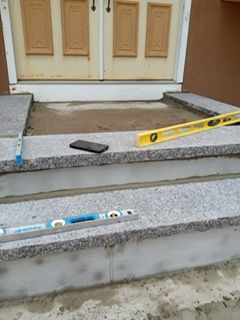 Granite steps under construction near a front door; levels and a phone sit on the steps.