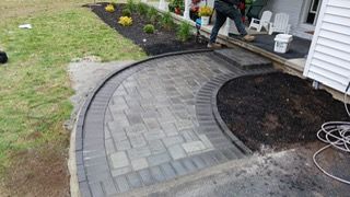Brick walkway leading to a porch with a person, mulch, and green grass.