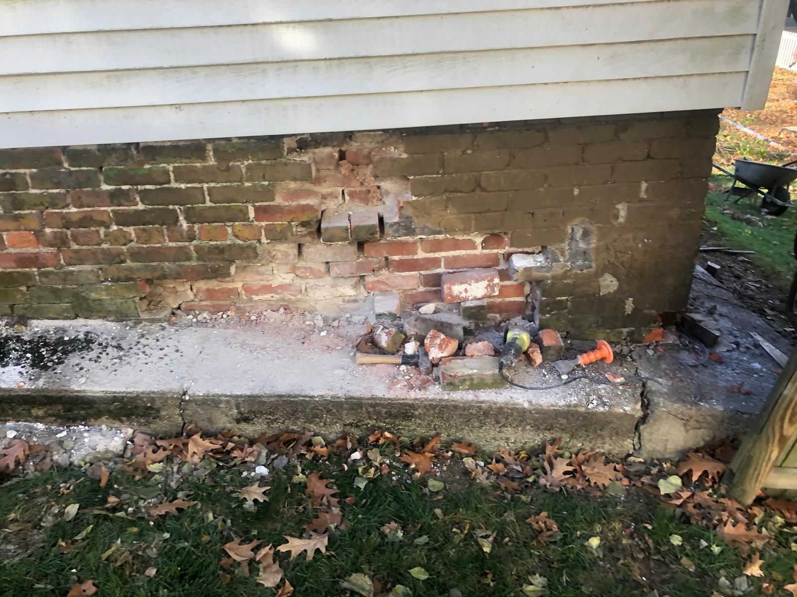 Damaged brick foundation of a house with debris on the concrete base and ground.