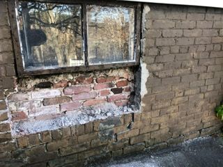 Window in a brick wall with damaged brick and crumbling mortar; exterior view.