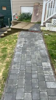Brick path leads to a house entrance with a ramp. Gray bricks bordered by grass.