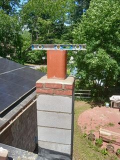 Chimney with a level on top, surrounded by trees and a red brick patio.