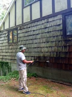 Man pressure washing a wood shingle house, removing dirt and grime from the exterior.