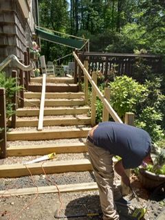 Person working on wooden stairs, building railing outdoors.