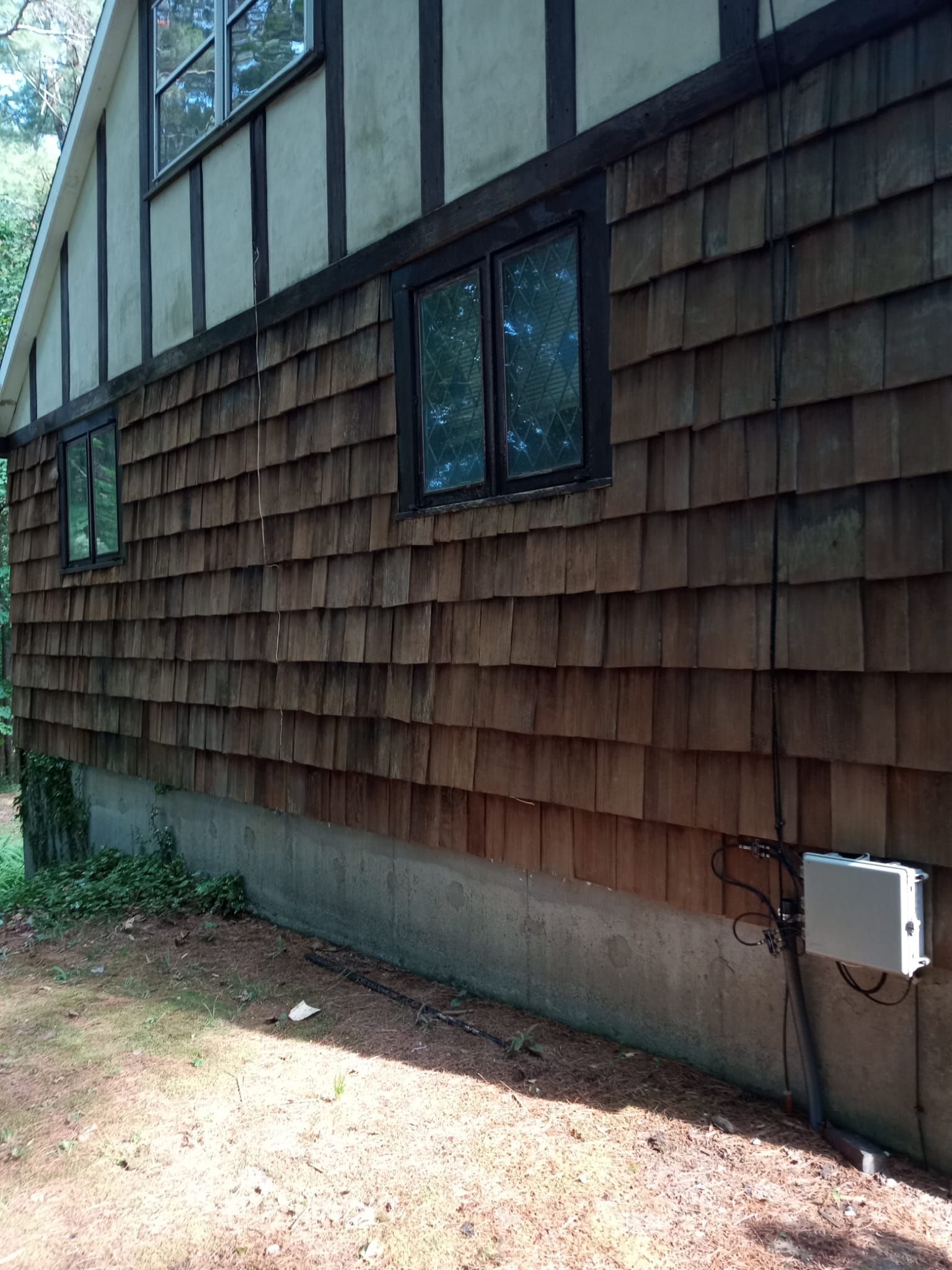 Brown wooden shingle siding on a house with windows, against a concrete foundation.
