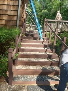 Brown wooden outdoor staircase with gravel, handrails, and a ladder. A person is working.