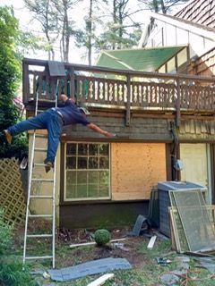 Man falling from a ladder on a deck, about to hit the wooden side of a house.