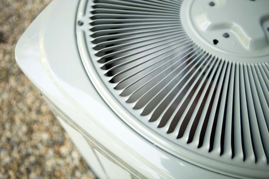 Close-up of a white outdoor air conditioner vent with gray fan blades and grilles