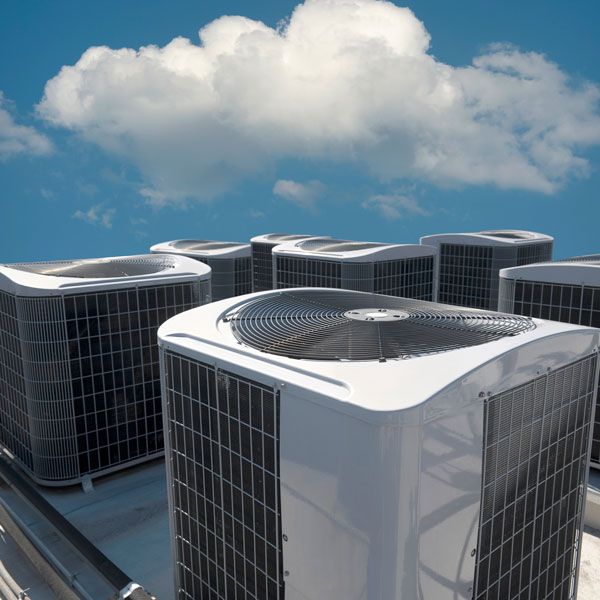Rooftop HVAC units with metal grilles under a blue sky with clouds
