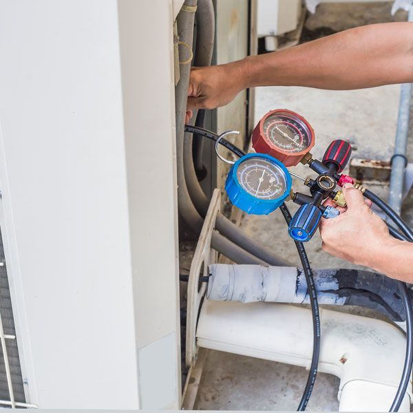 Technician using blue and red gauges to service HVAC pipes and unit outdoors