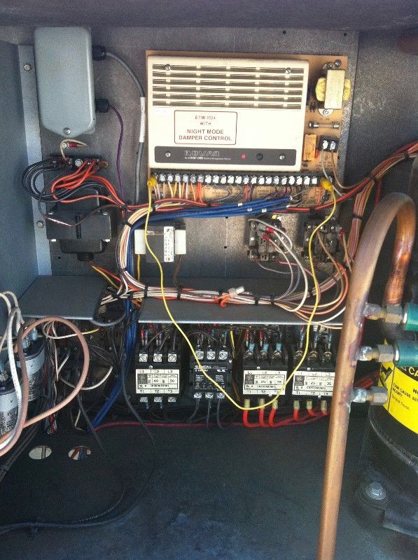 Open electrical control panel with wires, breakers, and a mounted device inside a cabinet.
