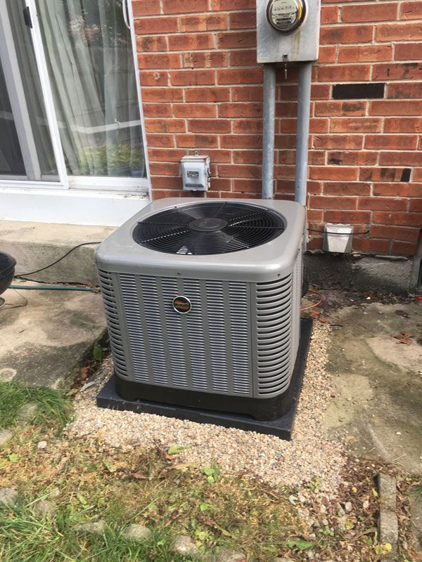 Outdoor air conditioner unit beside a brick house, with utility meters and a window nearby