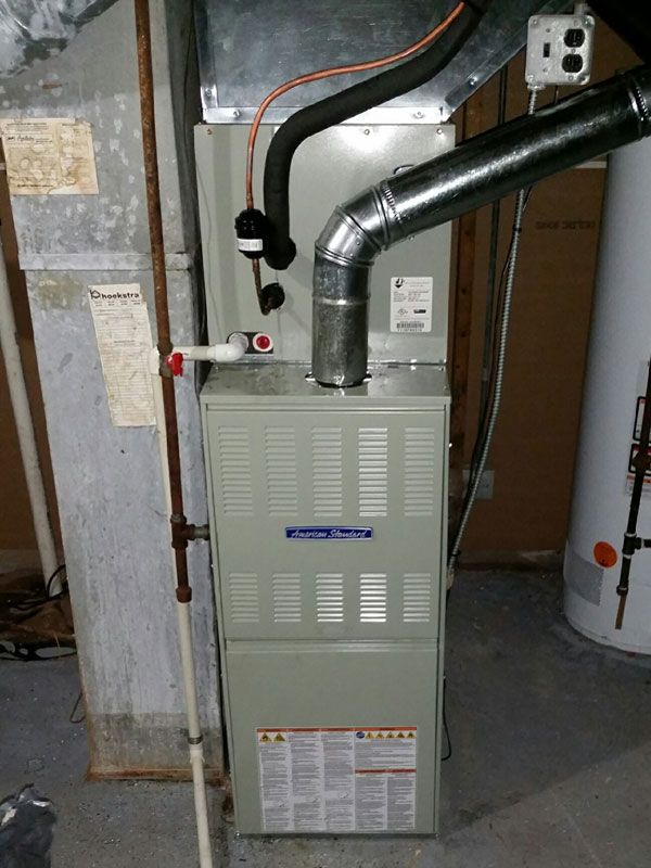 Furnace unit in a basement with silver ductwork and pipes attached to a concrete wall.