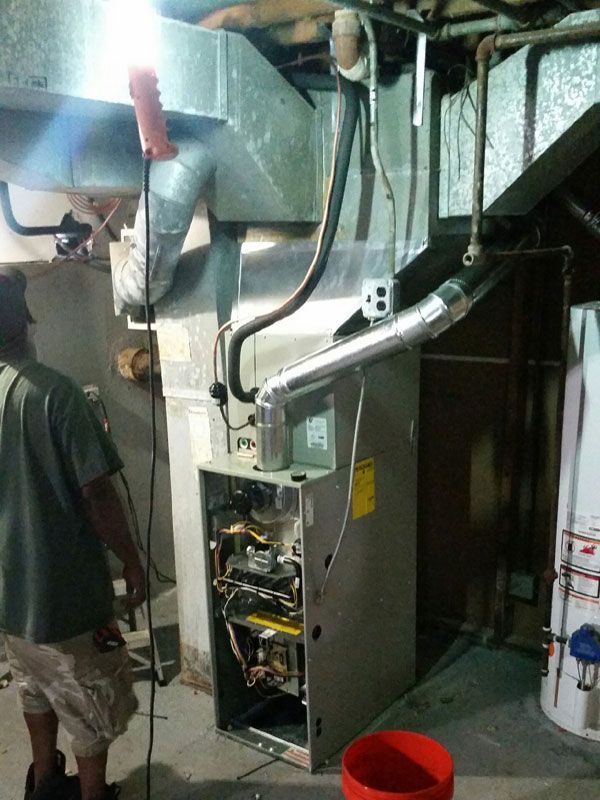 Basement HVAC furnace with open panel and exposed wiring next to a red bucket and laundry area