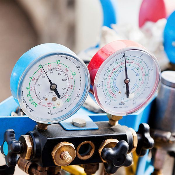 Blue and red pressure gauges on a valve manifold with blurred workshop background
