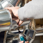 Hands pouring liquid from a metal pitcher into a polished stainless-steel coffee machine