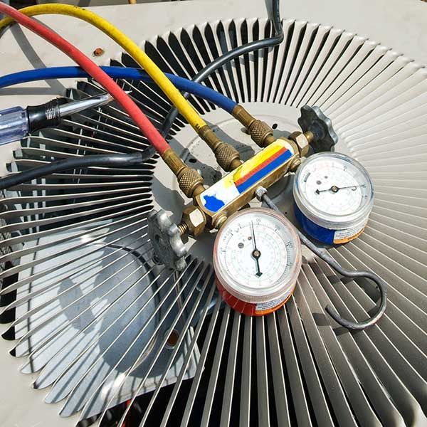 Dual pressure gauges and colored hoses connected to an air conditioner condenser coil.