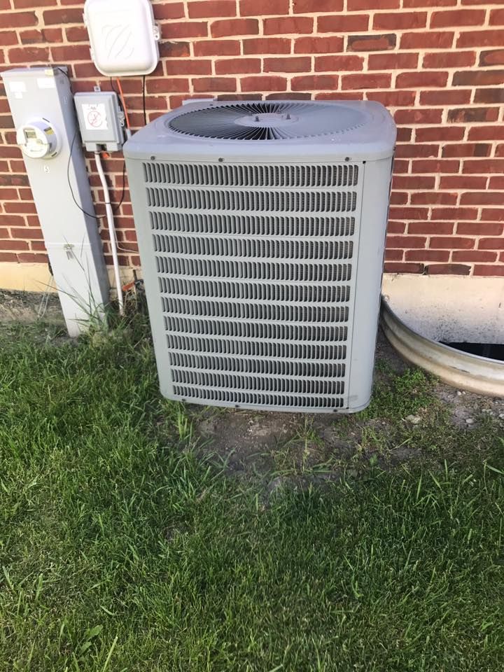 Outdoor air conditioner unit beside a brick house wall with grass in front.