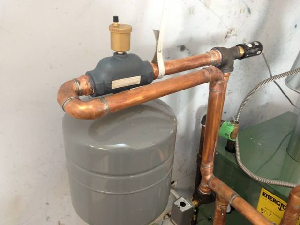 Copper pipes and black valve assembly above a gray water heater in a utility area