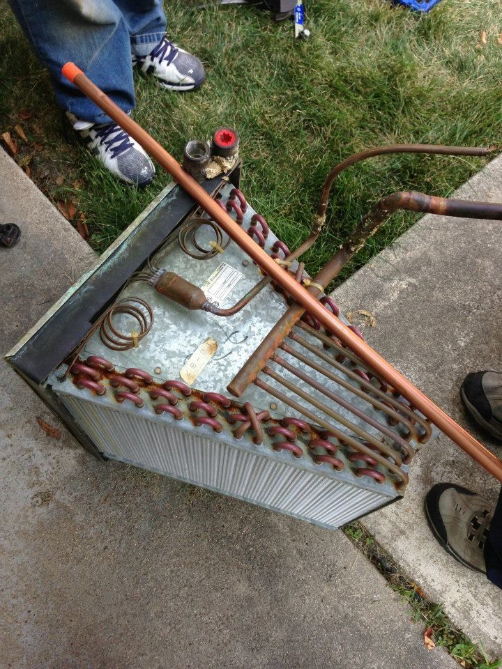 Person holding a long-handled tool over a metal radiator on a sidewalk, with hoses and equipment nearby