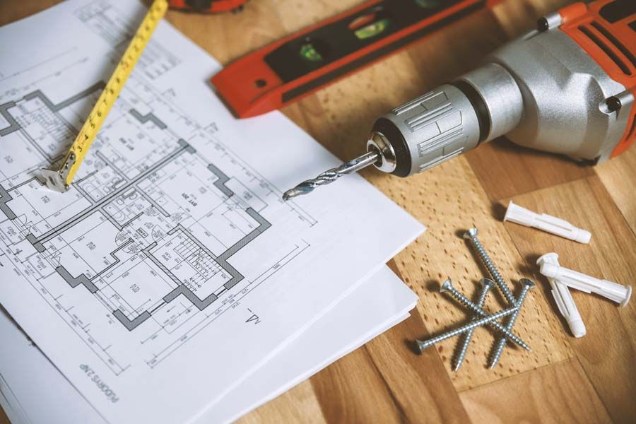 Blueprints, drill, level, and screws on a wooden workbench for home renovation planning