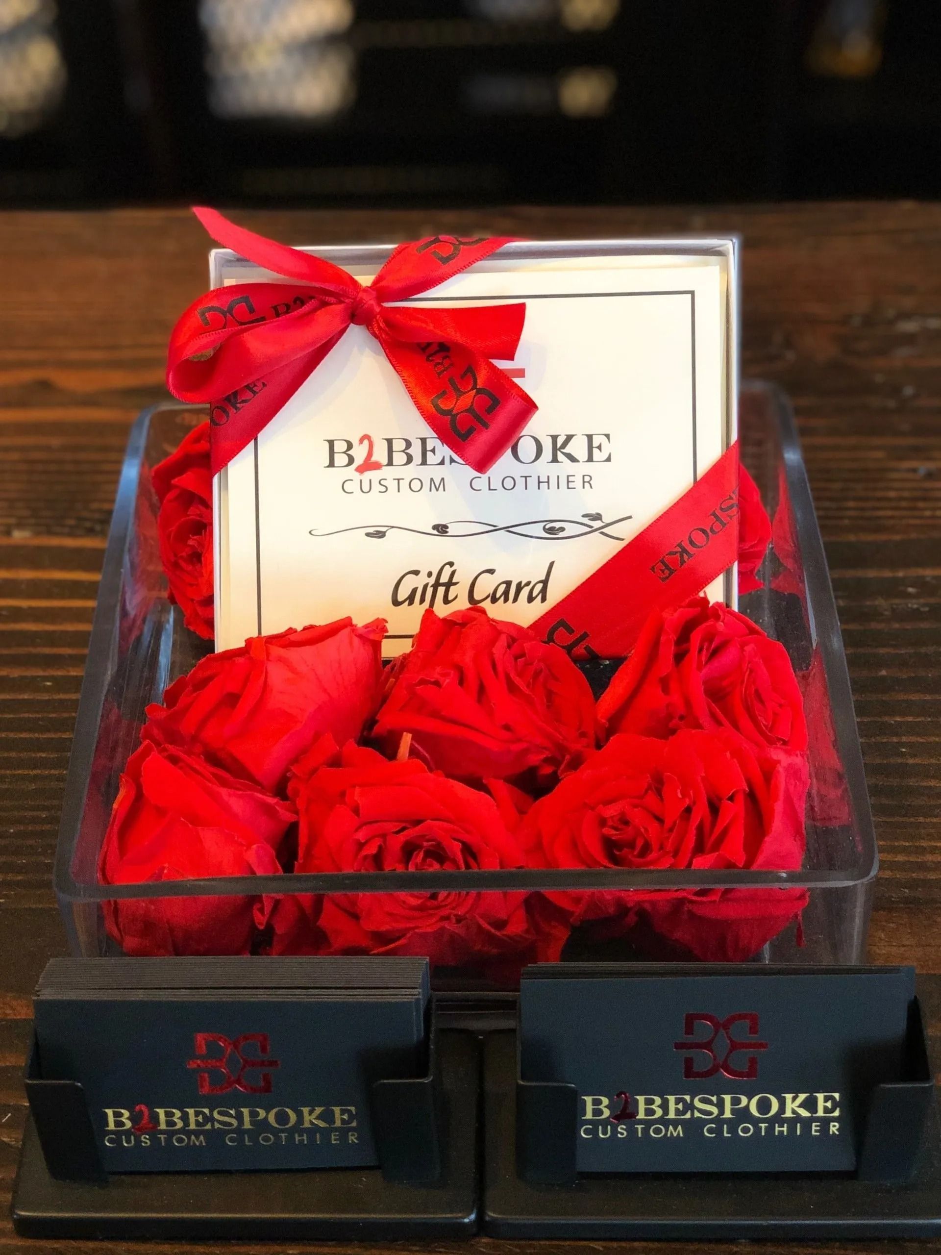 Gift card and red roses in a clear display. Business cards in black holders on a wooden surface.