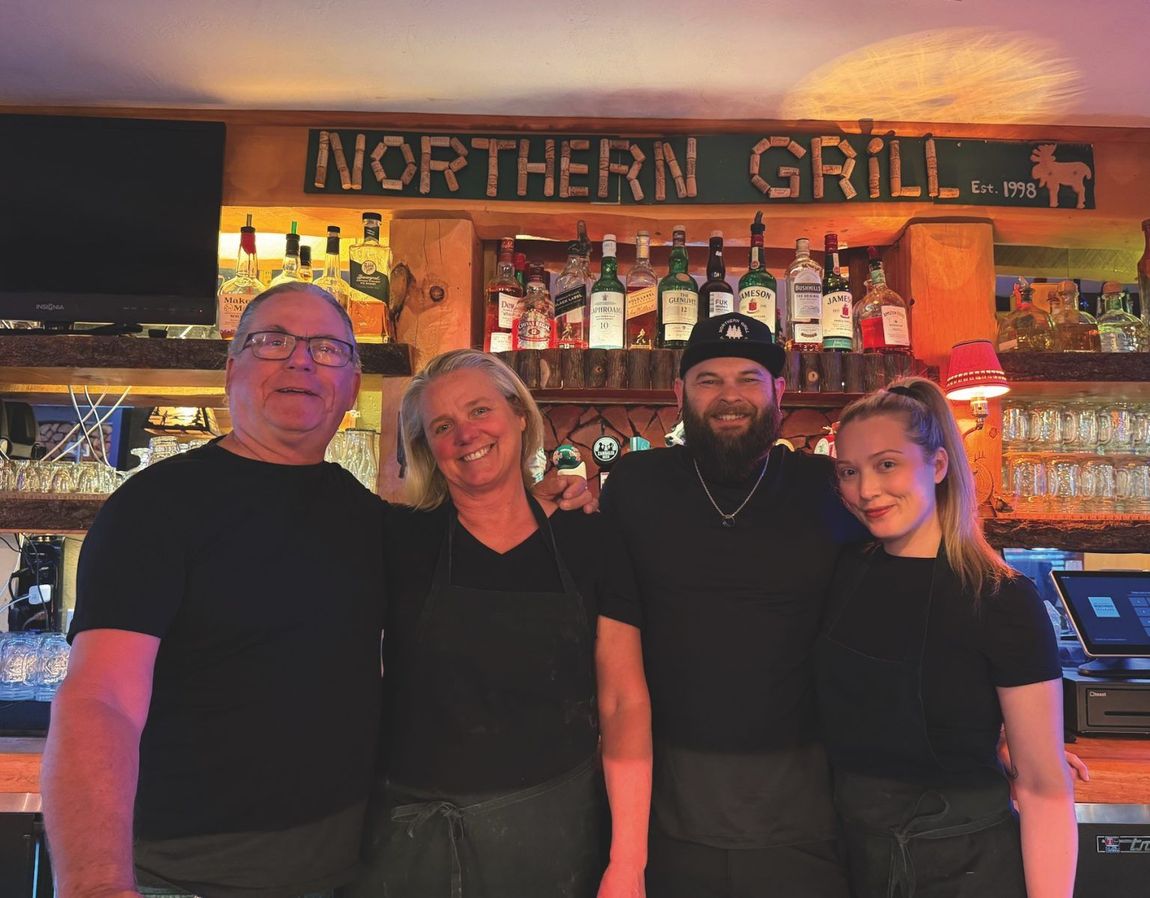 Four people posing at a bar with a “Northern Grill” sign and bottles displayed behind them.