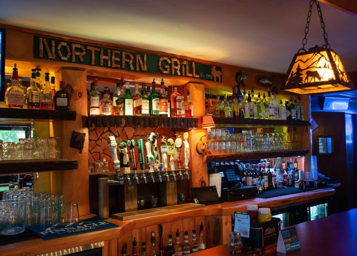 Warmly lit Northern Grill bar with shelves of liquor bottles and wooden counter פנים