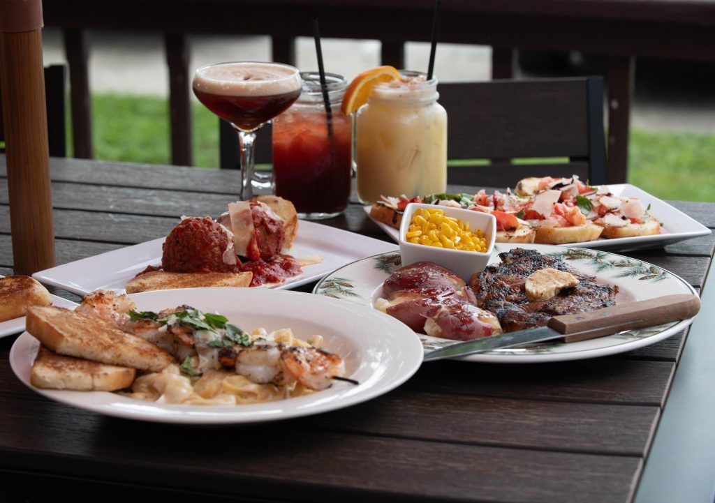 Outdoor table with assorted plated dishes and drinks, including a cocktail and a dessert glass.