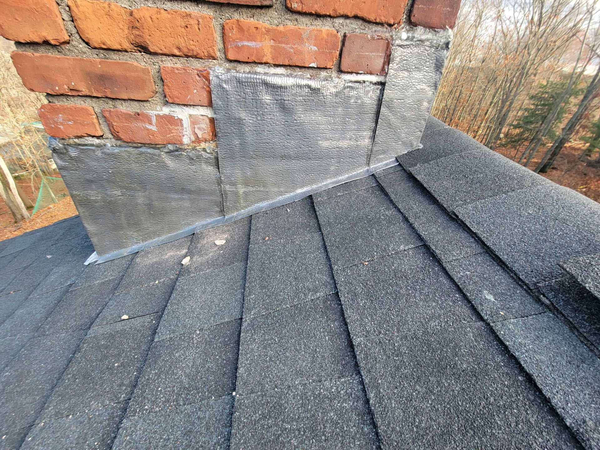Roof shingles and chimney base with flashing, showing a close-up of roof repair details.
