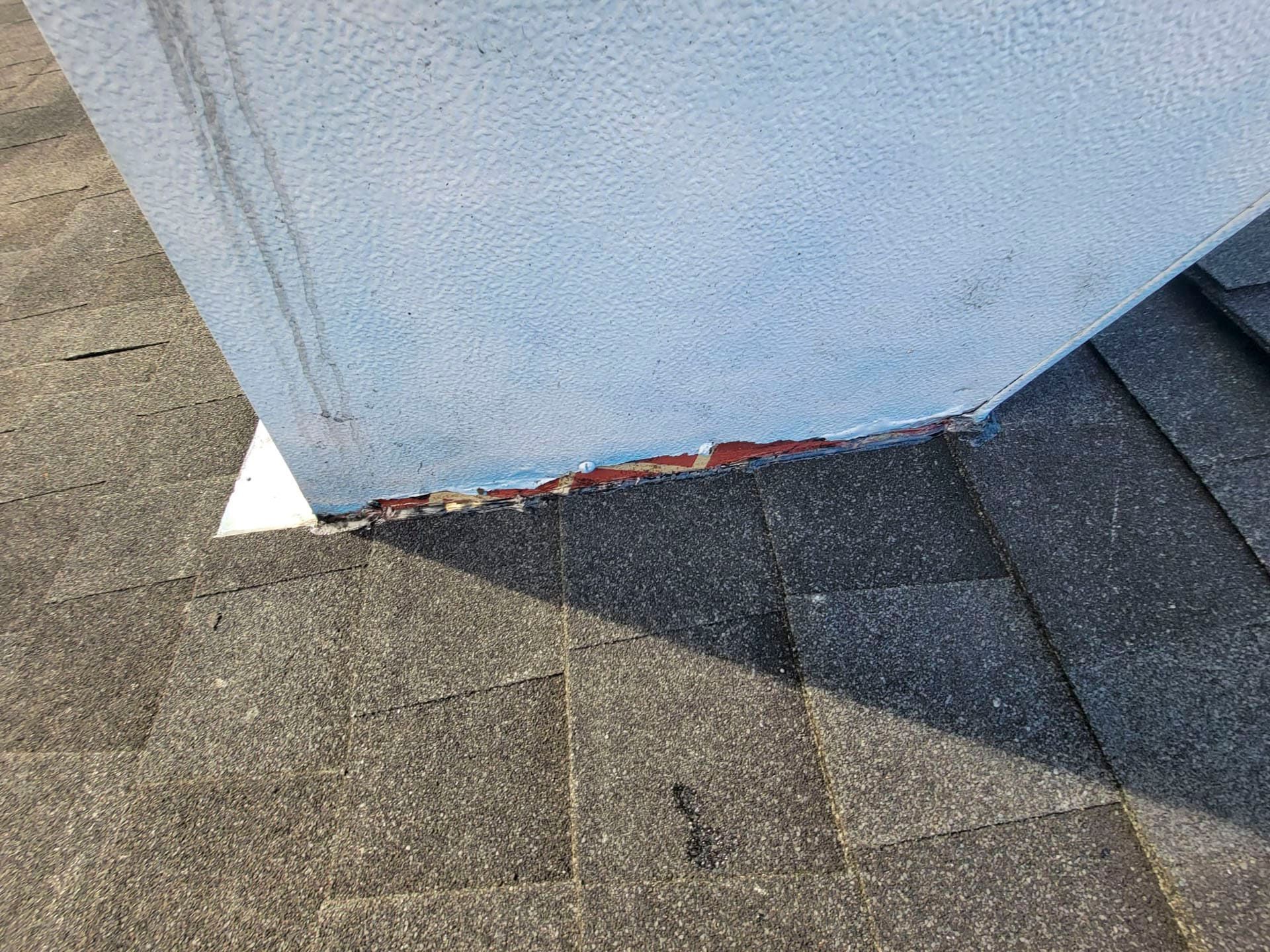Damaged white building corner above roof shingles, with peeling paint and exposed red trim at the base