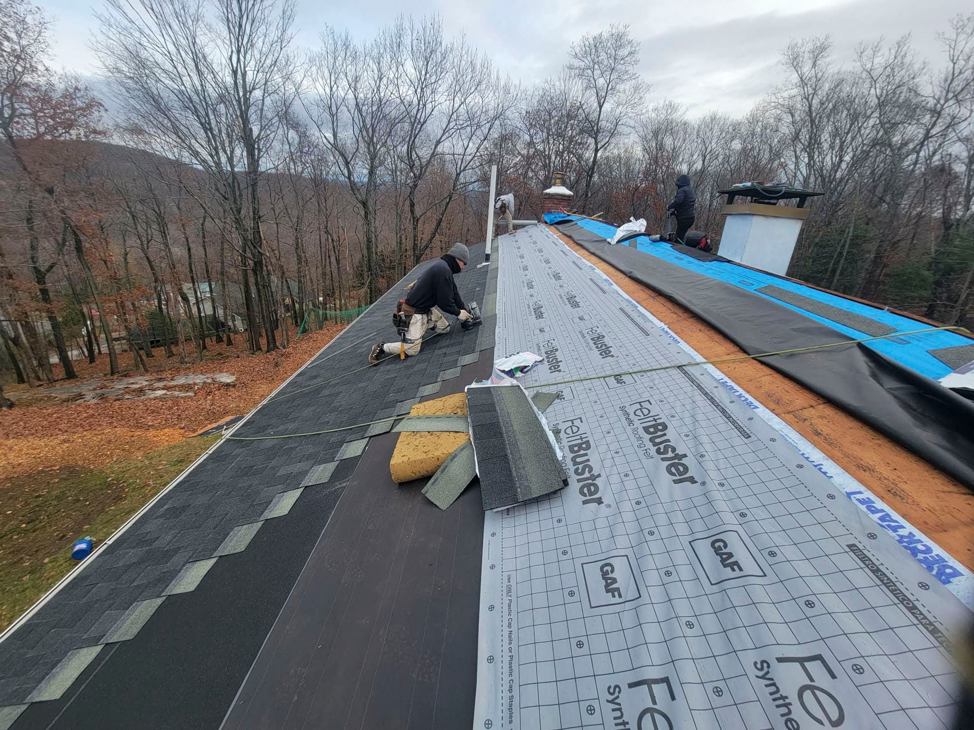 Roofing work in progress on a sloped roof, with workers and underlayment visible.