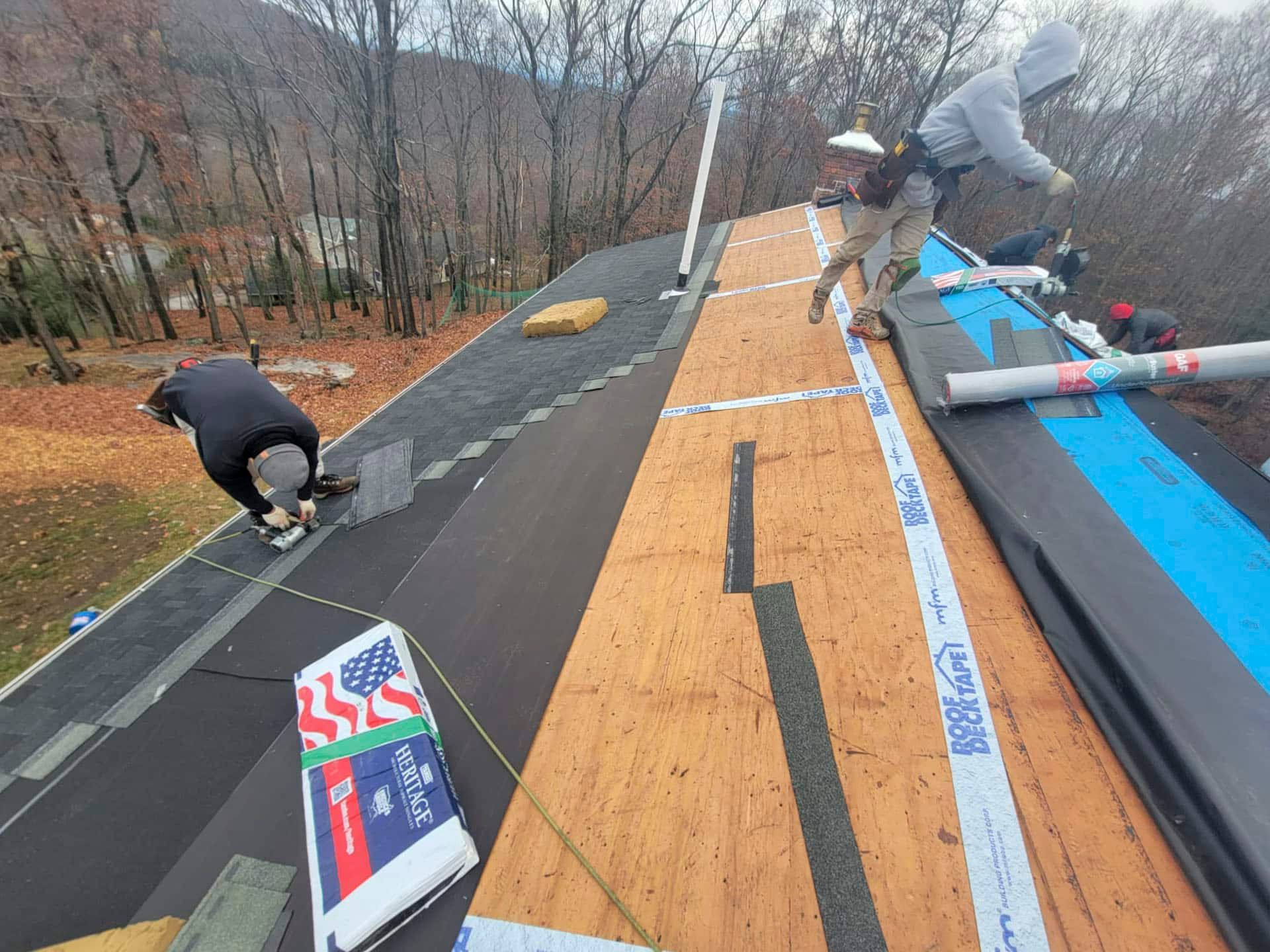 Workers installing rooftop shingles and underlayment on a house roof in autumn.