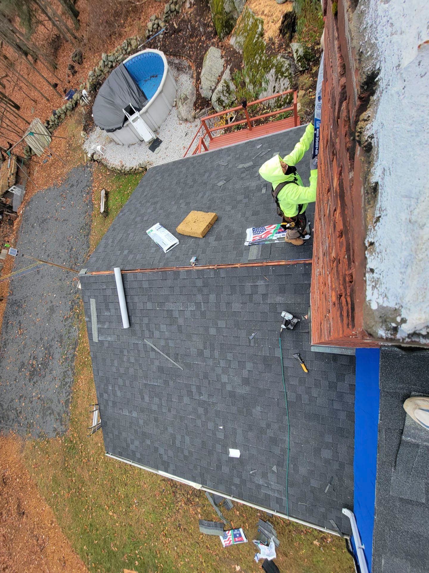 Roof repair in progress on a dark shingle roof beside a blue wall, with tools and materials nearby.