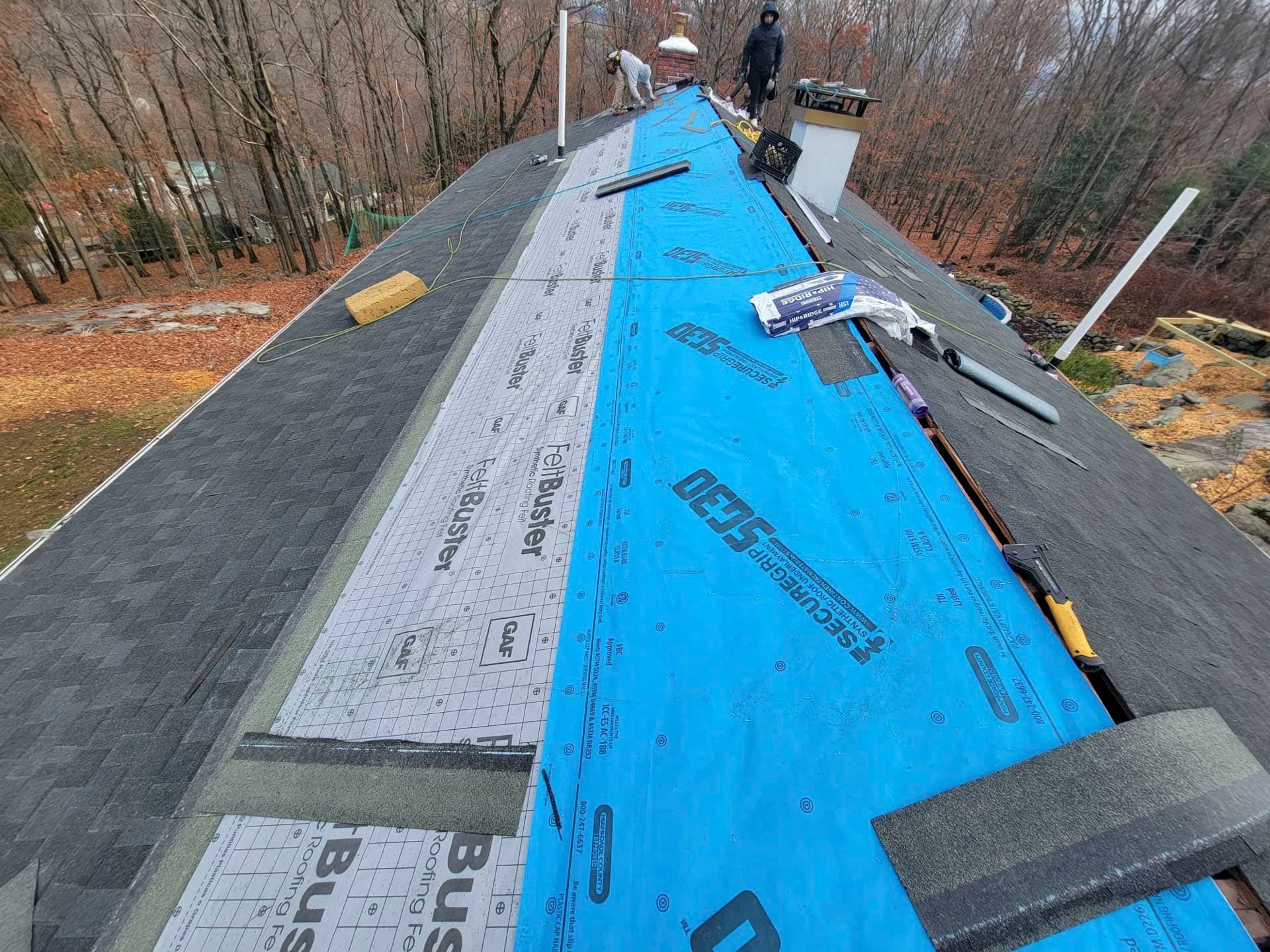 Roof under repair with blue underlayment and gray shingles on a steep slope