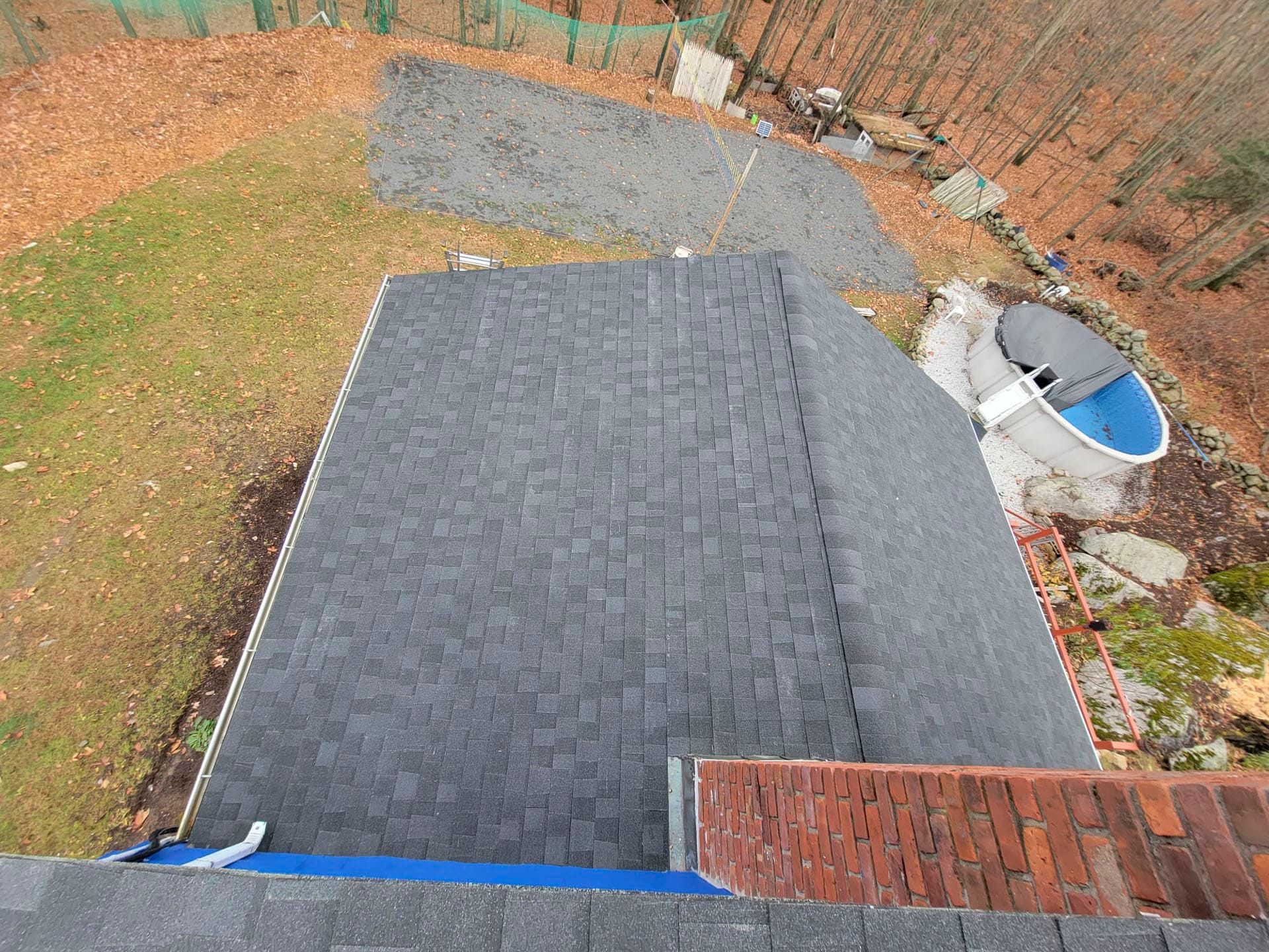 Rooftop with dark shingles beside a gravel area, brick wall, and a blue satellite dish in a backyard.