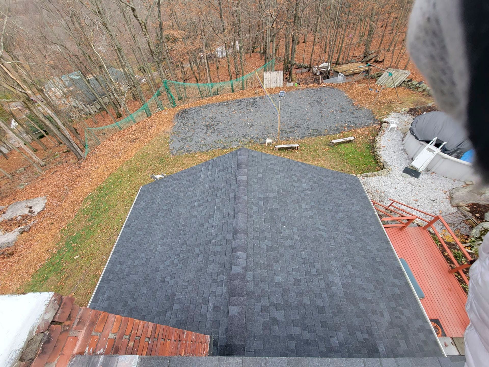 Rooftop view of dark gray shingles and a gravel yard with bare trees in fall.