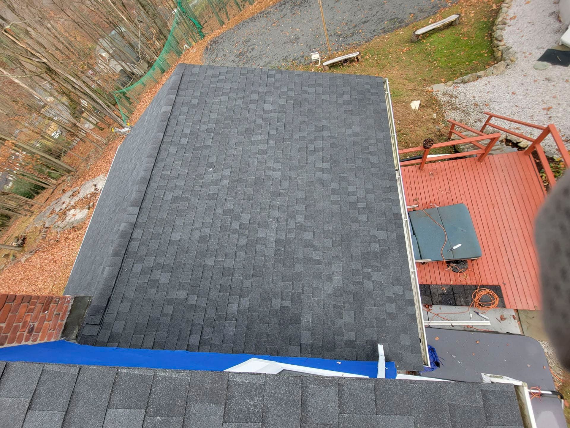 Roof and backyard view with a dark shingled roof beside a red patio and gravel path