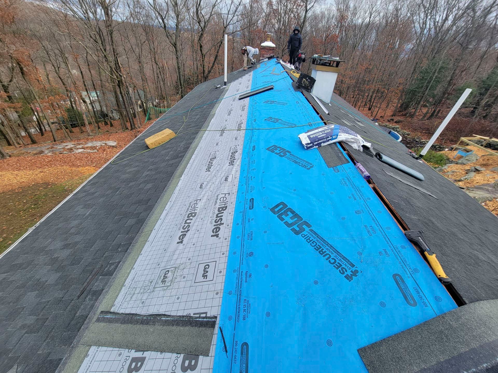 Roof under repair with blue and gray roofing underlayment on a steep house roof.